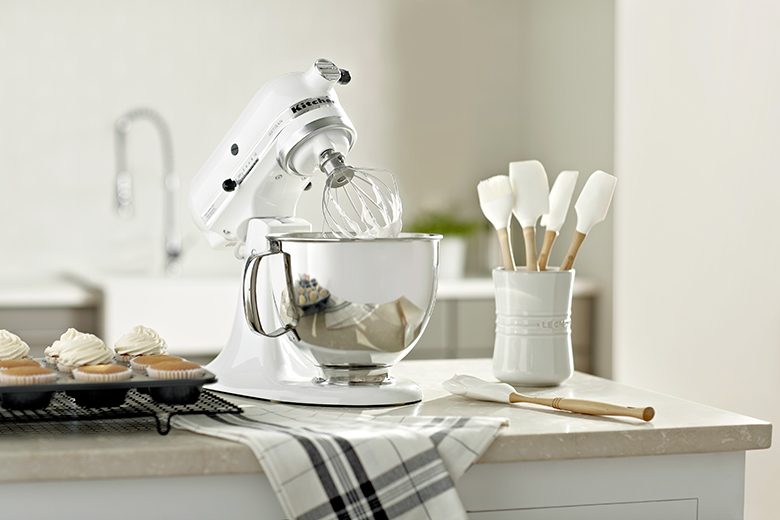 kitchen scene with frosted cupcakes, white KitchenAid stand mixer, white Le Creuset utensil crock with silicon spatulas on the counter