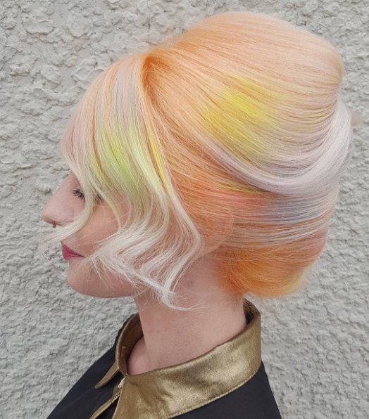 woman with blond and orange sherbet colored hair with bright yellow and darker orange patches, pulled back into a voluminous french twist, with a loose long bang sidepart for a wedding hairstyle