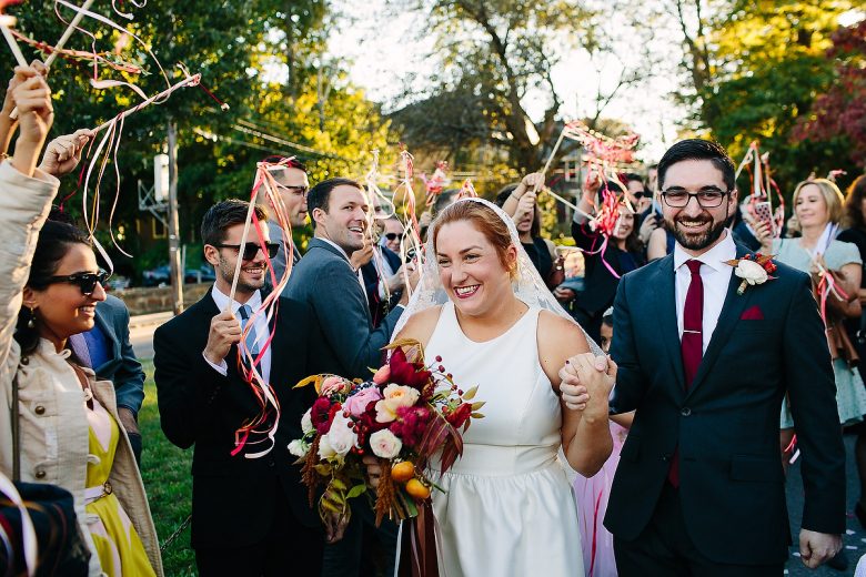 Bride and groom walking among guests holding colorful streamer wands