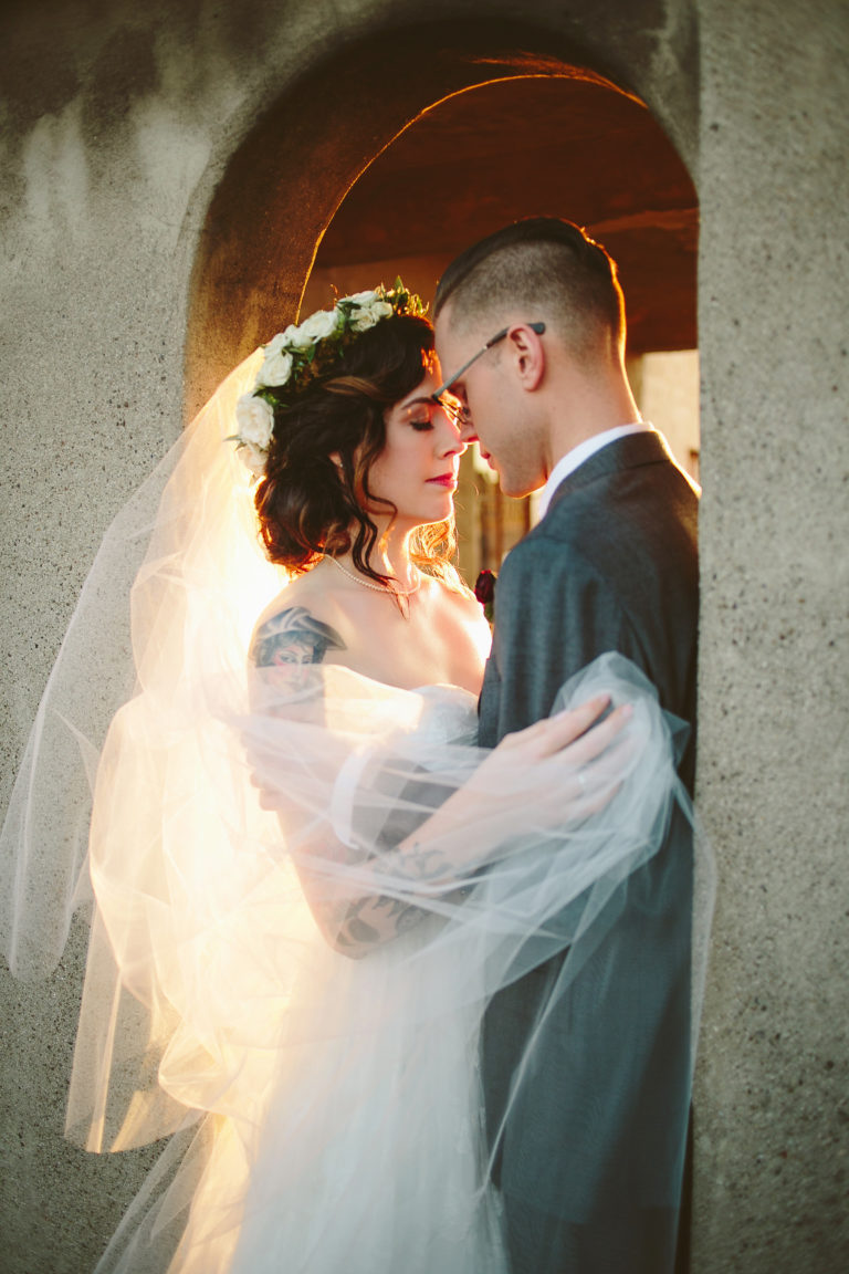a wedding couple embraces in a doorway with foreheads touching as the sun bathes them in an orange glow