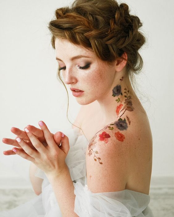 woman with flower tattoos from neck down shoulder with red hair in loose horizontal braid crown and braids gathered on top of her head