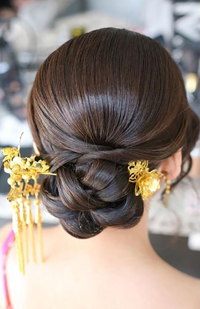 woman with sleek dark hair pulled back into woven twist with large gold floral pin