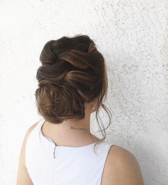 woman with hair loosely braided and woven on the top of her head, then gathered at nape for a wedding hairstyle
