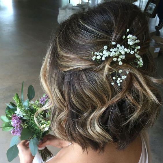 Woman with chin-length hair in loose waves, gathered half up with baby's breath for a wedding hairstyle