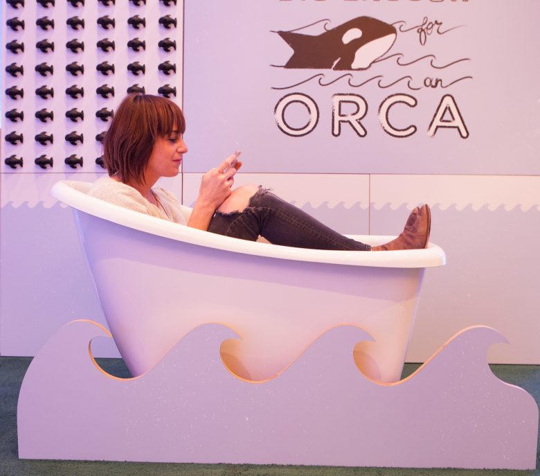 Woman sits in a bathtub, fully clothed, texting.