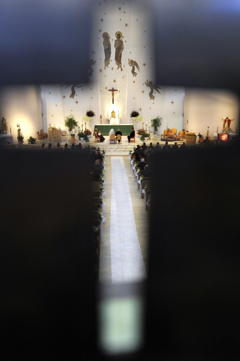 View of a church ceremony while peering through the cutout outline of a cross