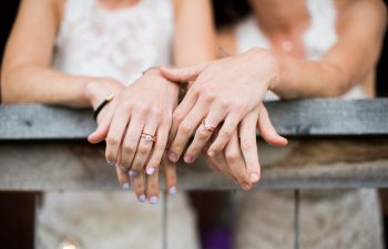 Two brides' hands together showing their wedding rings