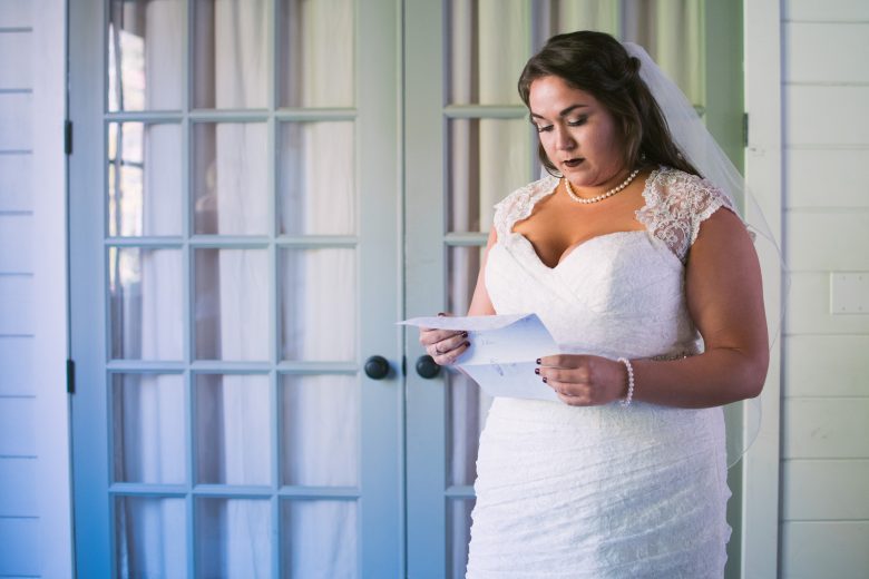 bride reads an unfolded piece of paper in front of closed french doors