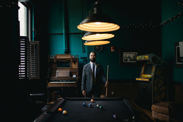 man in suit holding pool stick in front of pool table in bar