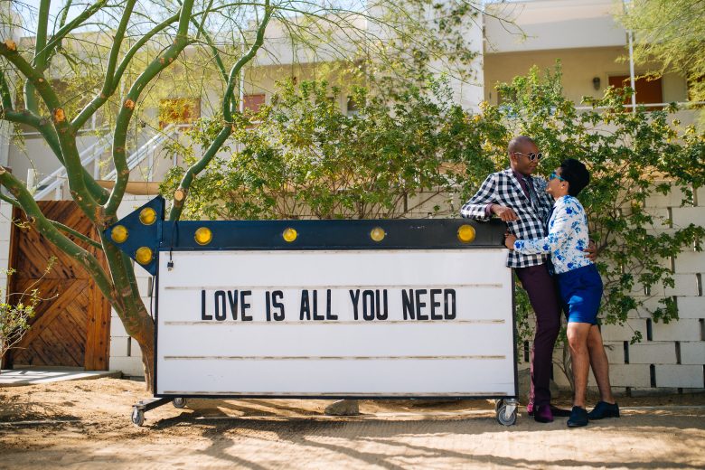 couple leaning on a letterboard sign with arrow that reads Love is all you need.