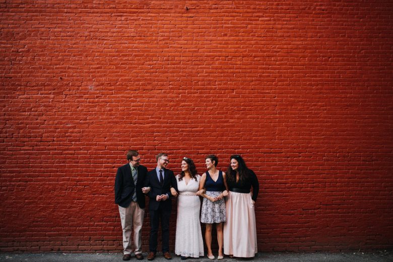 wedding party with bride in center in front of red wall