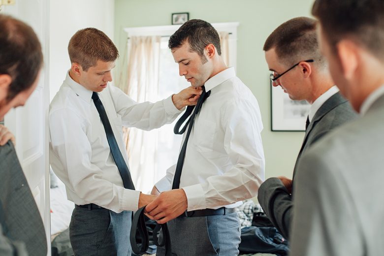 Wedding party of men getting dressed, tying their ties.