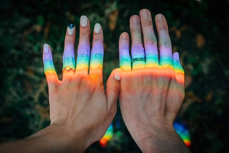 Closeup of two hands with new wedding rings, a rainbow shining across 