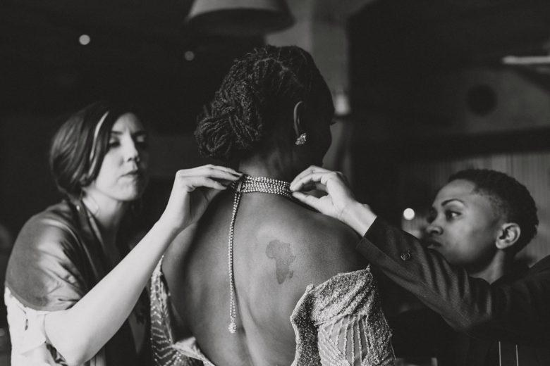 Women assist a bride as she puts on her wedding jewelry