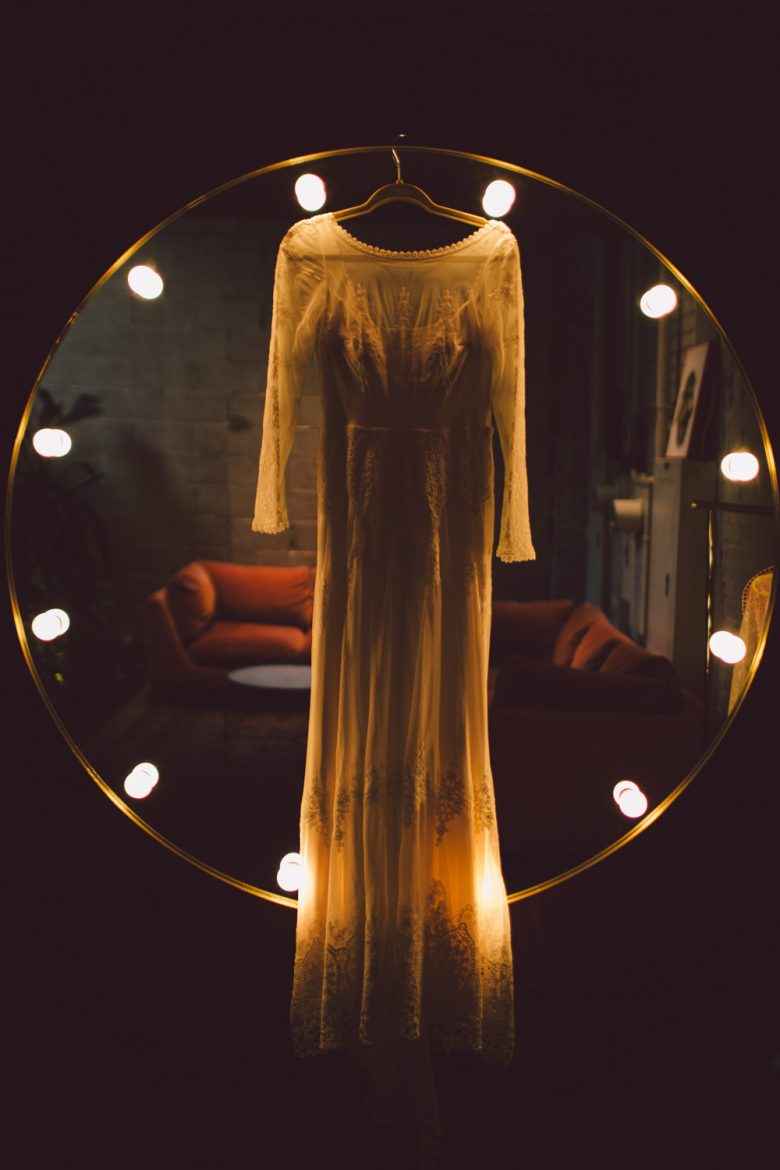 A wedding dress hangs in front of a mirror