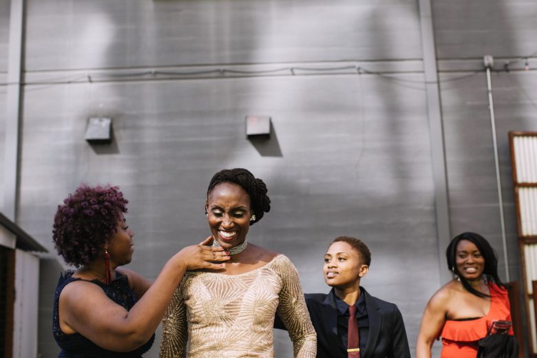 A bride smiles as her wedding party adjust her outfit with final touches