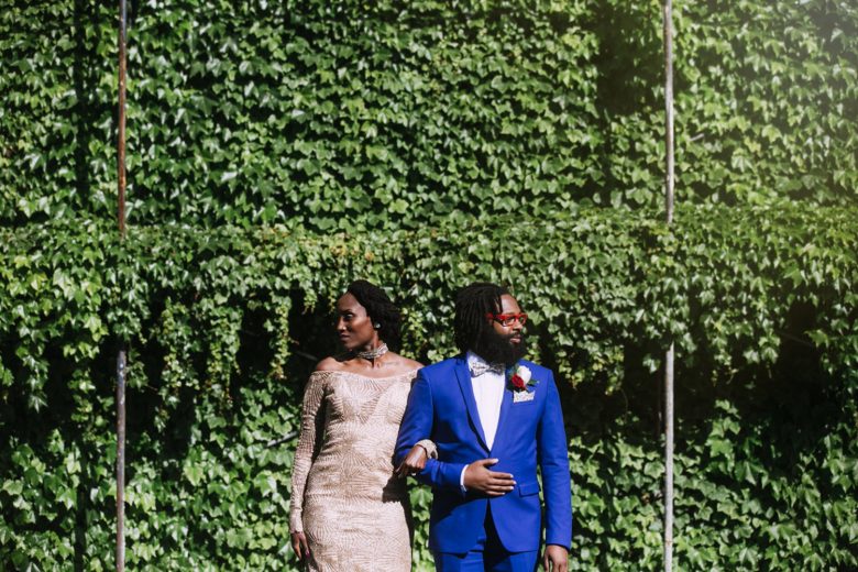 The wedding couple pose in front of a giant wall covered in greenery