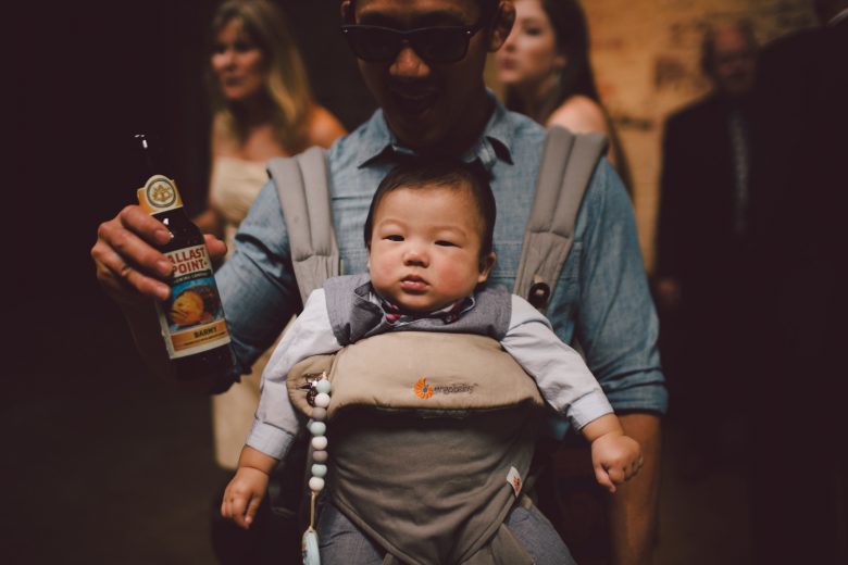 closeup of a baby sitting in a front facing baby carrier worn by a male person