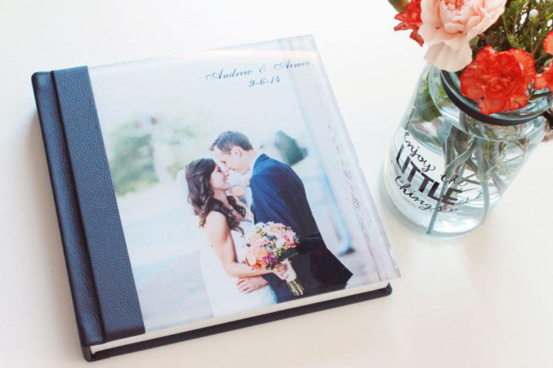 hardcover wedding album with solid black spine and photo cover next to a vase of flowers that reads enjoy the little things