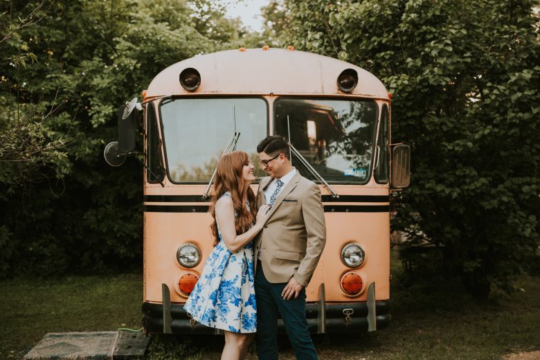 Couple in party clothes smiling at eachother, standing in front of a vintage bus