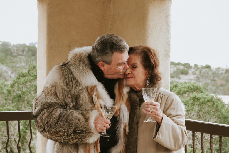 man in heavy fur coat kissing woman on the cheek, both hold champagne gobblets