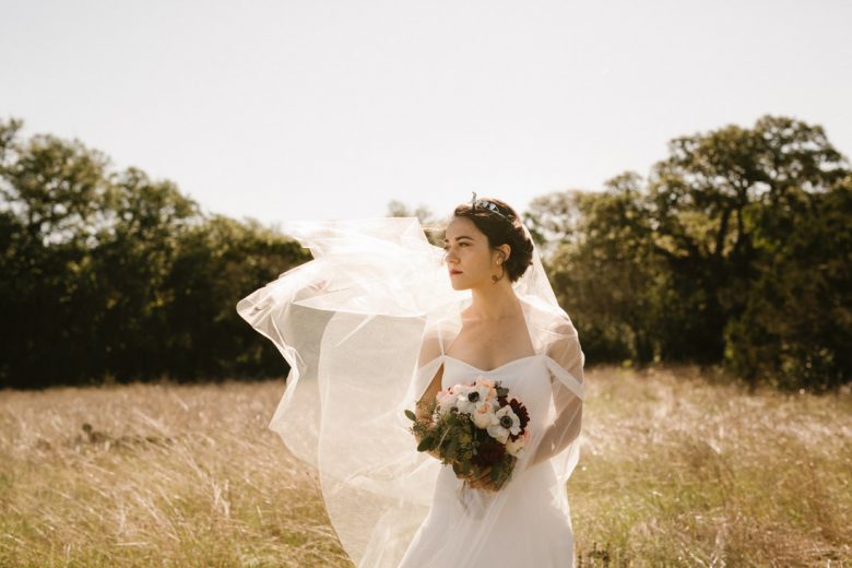 bride looking off to the left in a field, her veil billowing in the wind
