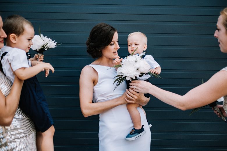 bride holding little boy ring bearer and bouquet in front of blue wall