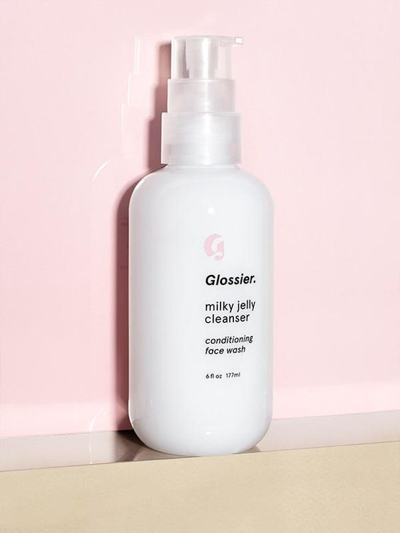 Glossier milky jelly cleanser bottle sitting on shelf against pink background