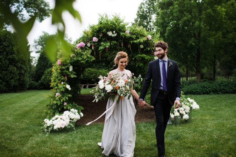 Bride and groom walking away from lush floral arch