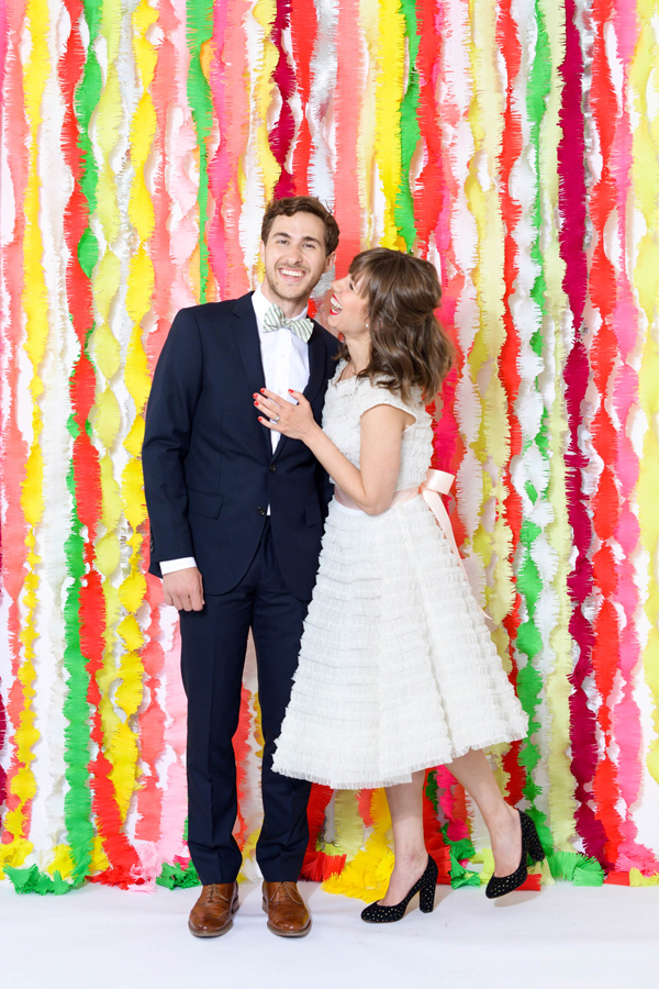 Bride and groom standing in front of a fringe streamer background wedding decoration.
