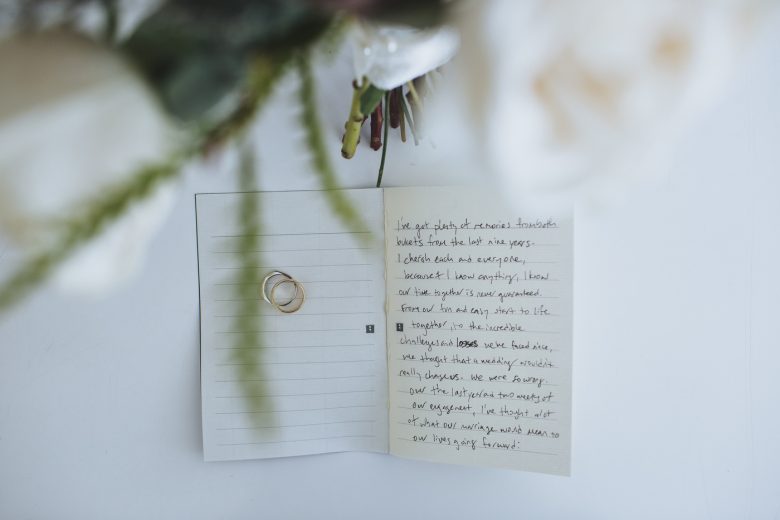 handwritten vows on small lined note pages, with wedding bands and a bouquet