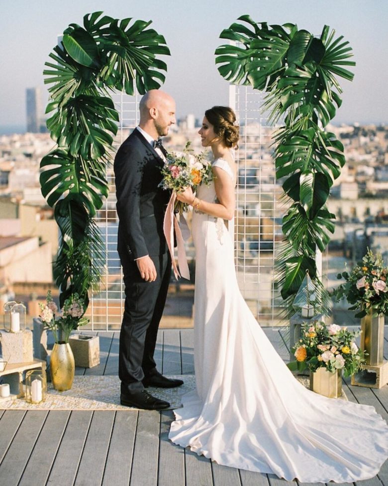 bride and groom at altar overlooking a cityscape bordered by large tropical leaves