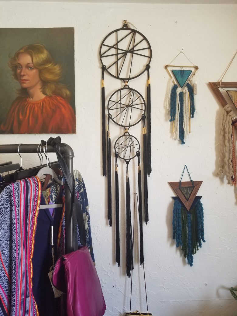 three tiered dreamcatcher against wall in boutique with other clothes and art