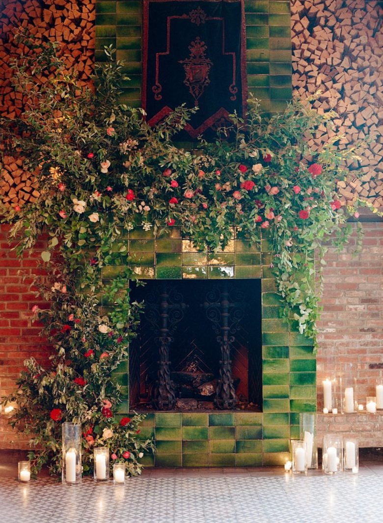 lush flowers and greenery overflowing from a mantle on a modern green ombre tile fireplace, down to the ground, surrounded by candles