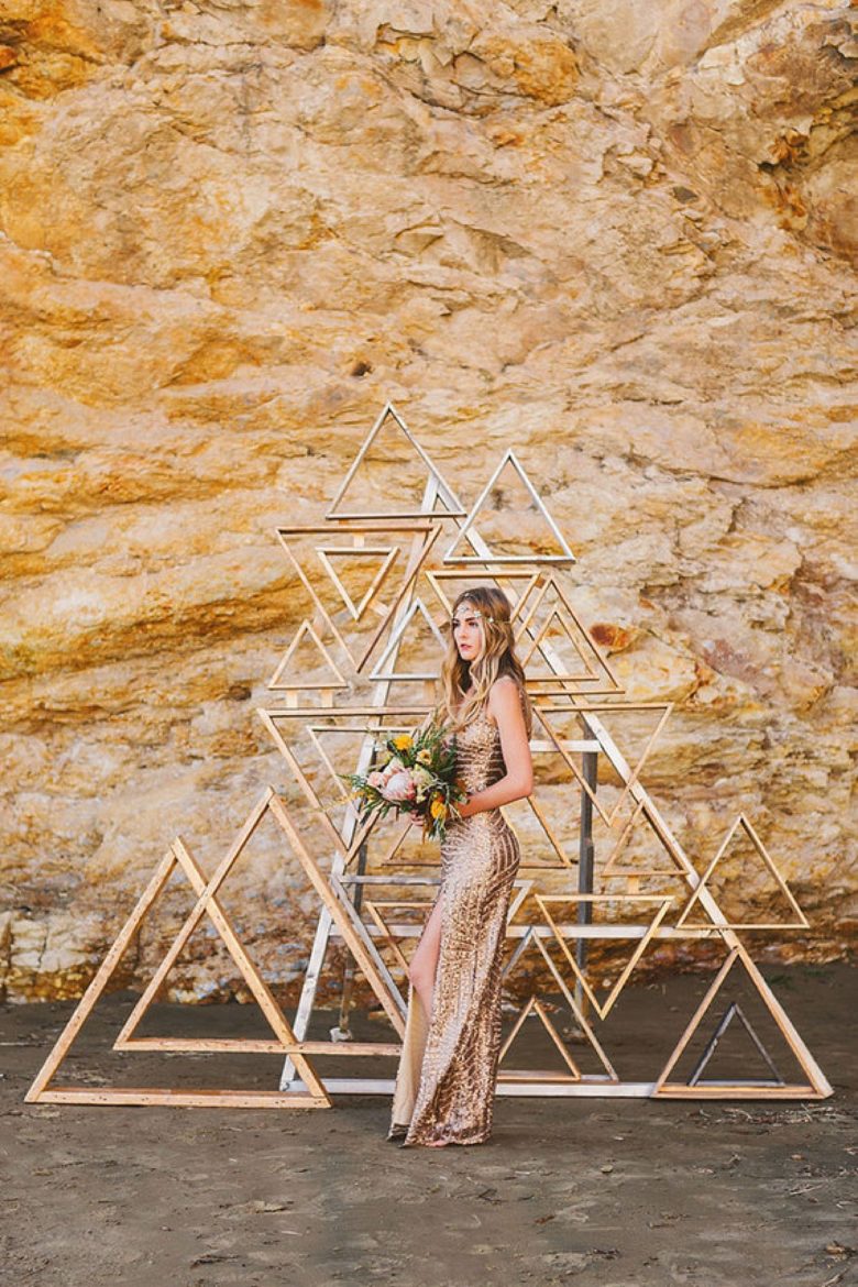 woman in sparkly gold cocktail-style dress stands in front of metallic triangle frame collage before a rock wall