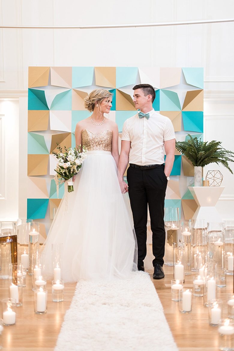 bride and groom hold hands in front of a geometric folded-paper style backdrop