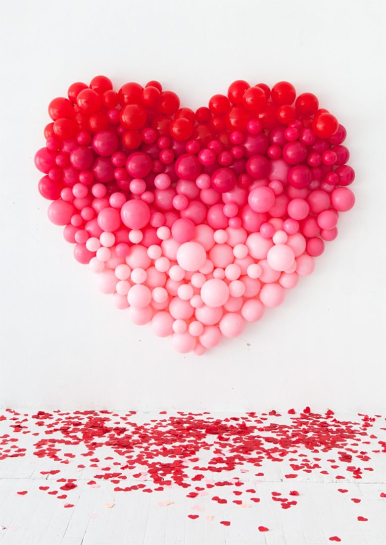 Ombre heart baloon sculpture hanging on white wall with cutout red and pink hearts scattered on the ground below
