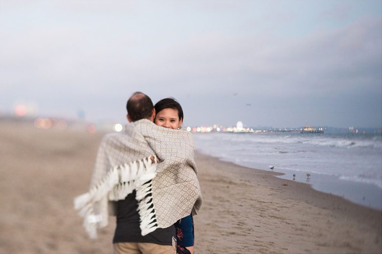 A couple embrace on the beach, wrapped up in a blanket
