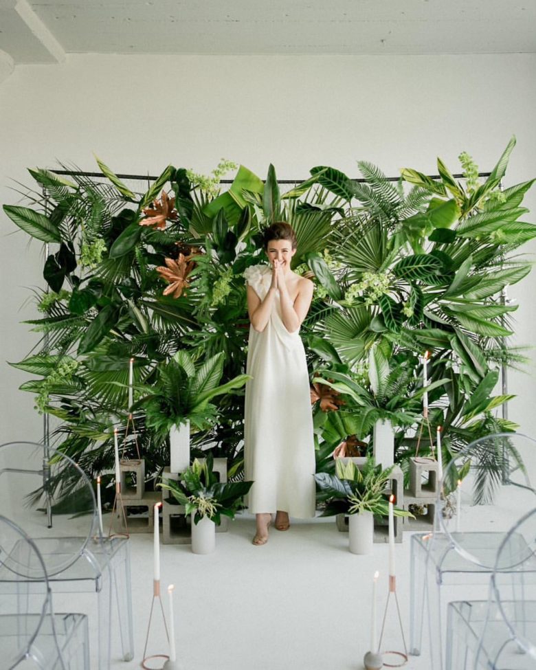 bride stands in front of lush backdrop of tropical greenery and flowers