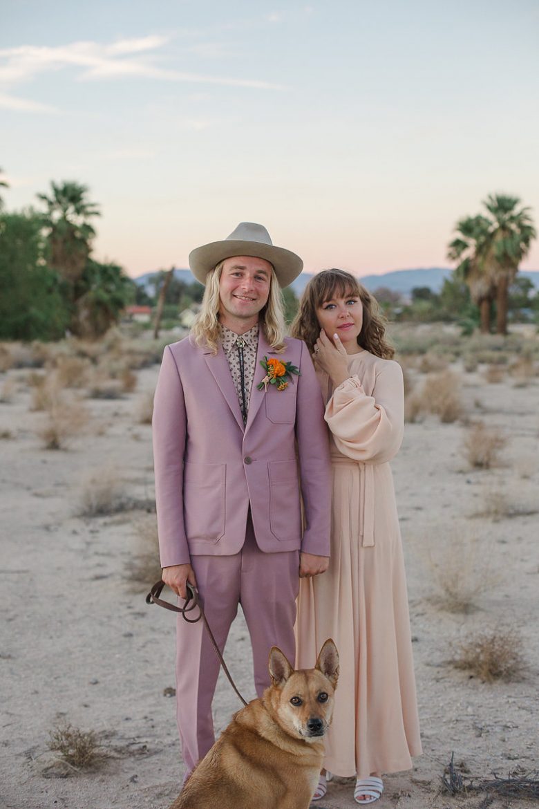 wedding couple in lavender suit and peach dress in desert with dog on leash in a Gina Clyne photo