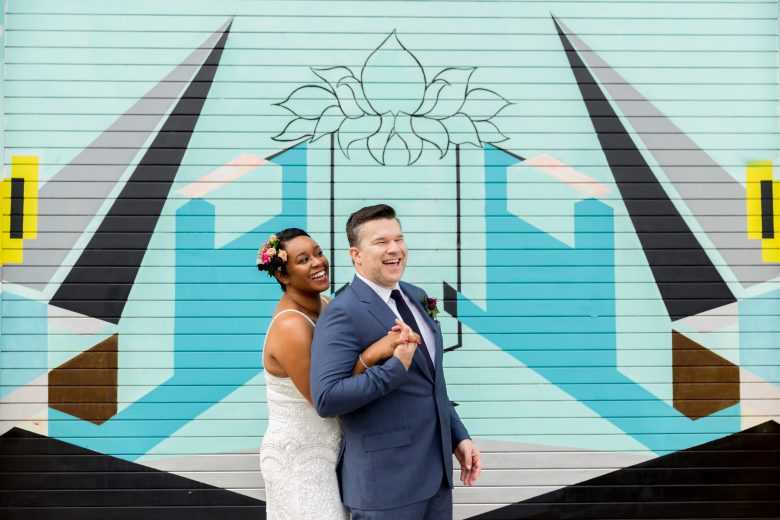 bride with colorful flower hairpiece and groom stand in front of a colorful graffitied wall
