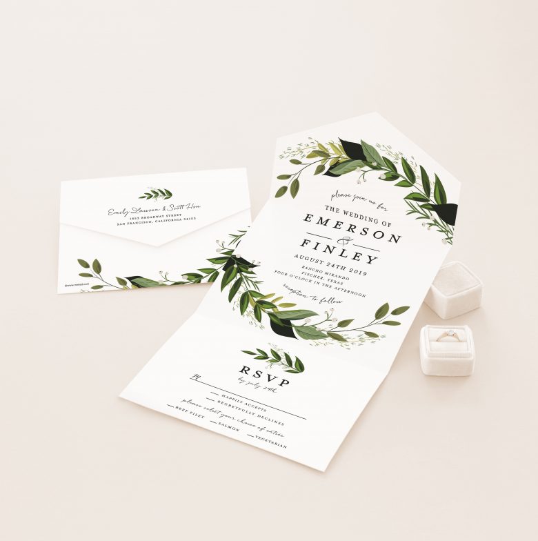 Green and white botanical all-in-one invite next to engagement ring