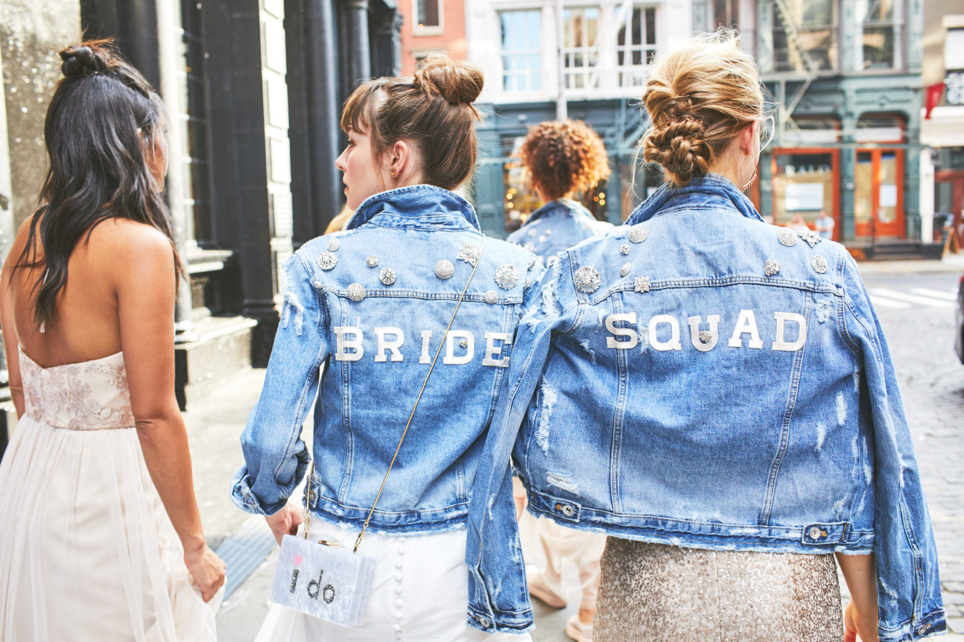 A bridal wedding party walk down the street wearing denim jackets
