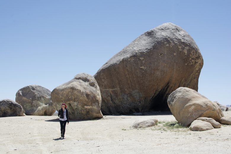 woman walking towards camera in desert with large rocks behind her