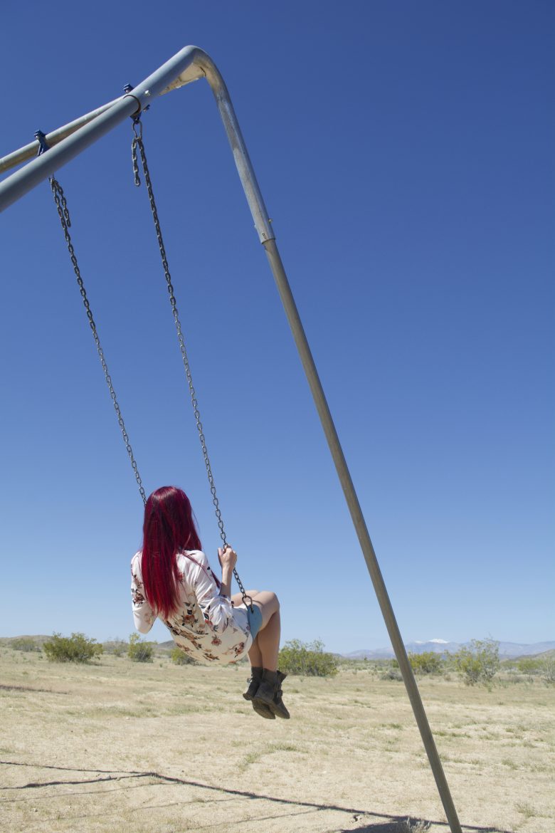 Girl on swing in desert against blue sky