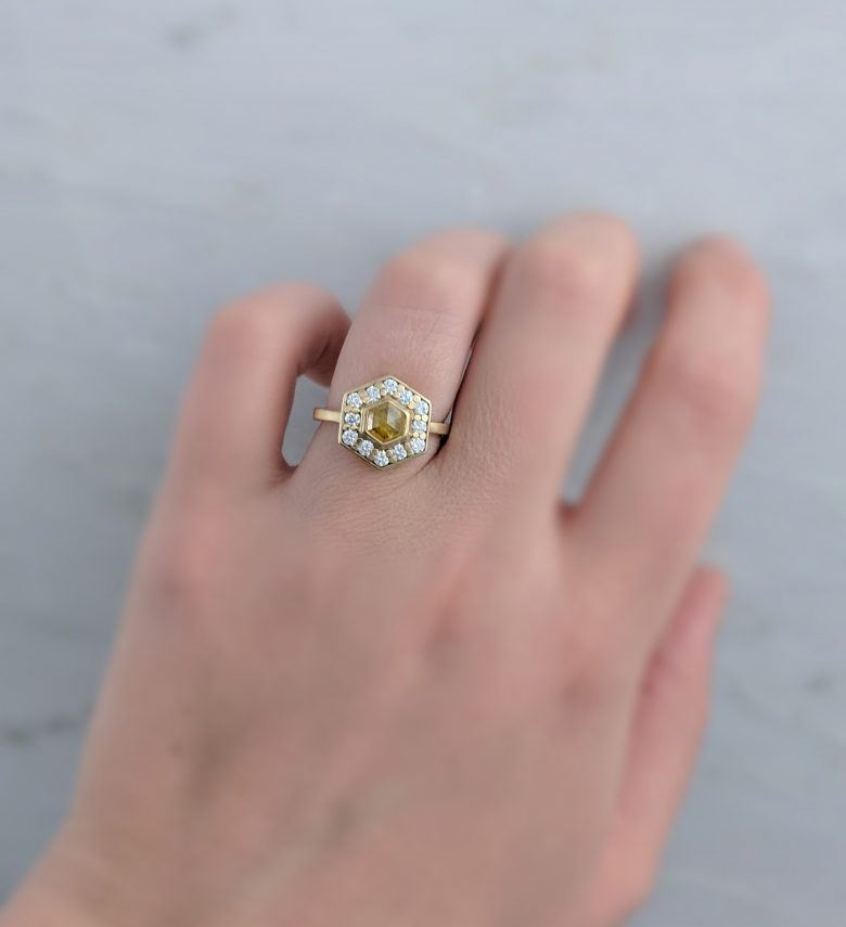 Hexagonal yellow gold ring with yellow stone surrounded by small diamonds on woman's ring finger