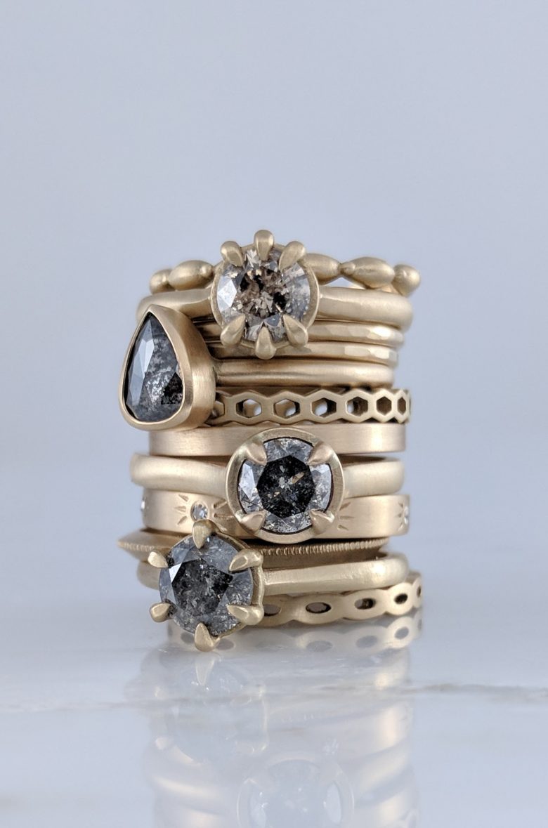 stack of rings, some with solitaire black and white speckled stones set in soft matte yellow gold