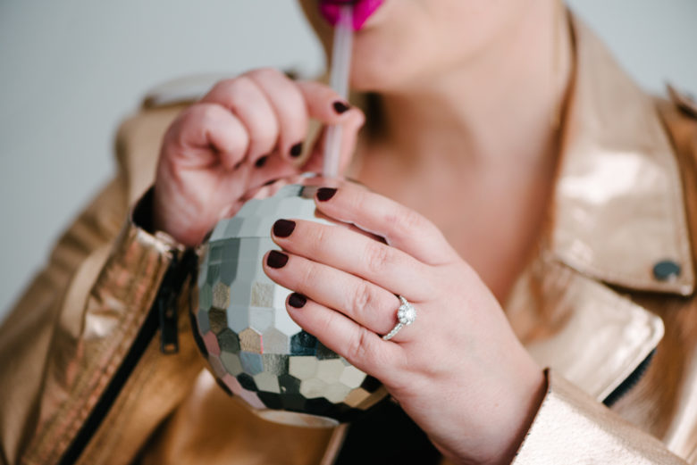 woman drinking out of a disco ball cup wearing a vintage inspired halo engagement ring