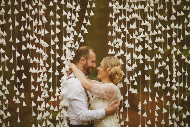 couple embraces among a waterfall-stylel of strings lined with tiny white paper cones