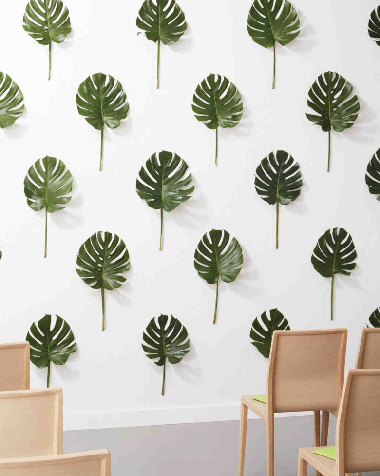 tropical leaves hung vertically on a wall and evenly spaced to create three-dimensional wallpaper-like pattern